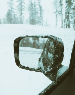 Car rear view mirror shows snow surrounding car , suggests danger