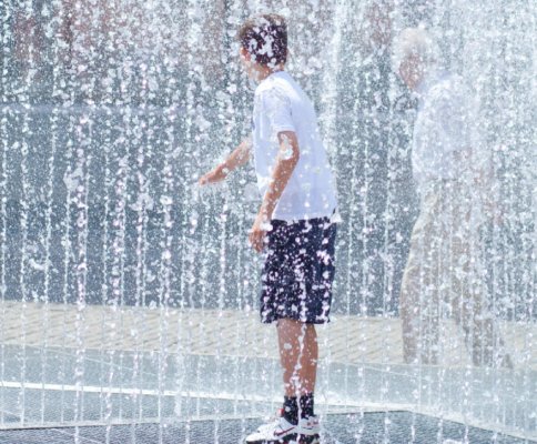 Young man standing in water fountain to avoid danger